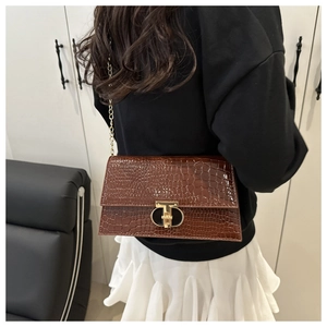 Macro detail of brown crocodile embossed shoulder bag with gold T-shaped lock on model