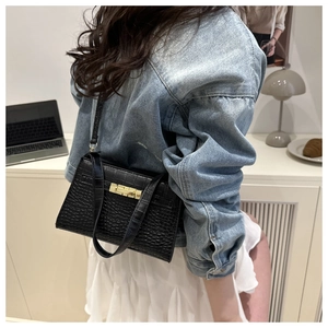 Detailed view of black crocodile pattern PU leather handbag with gold metal clasp on table