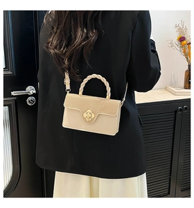 Detail view of beige crossbody bag with gold flower clasp and woven handle on model