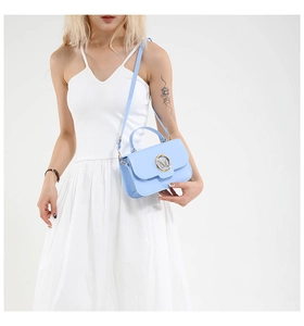 Detail of light blue mini bag with golden M metal logo worn with a white dress