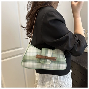 Detail of green checkered underarm bag featuring a brown bow and slim leather strap