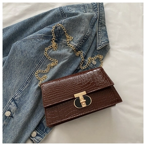 Detail of dark brown crocodile texture bag with golden T-shaped clasp and chain strap