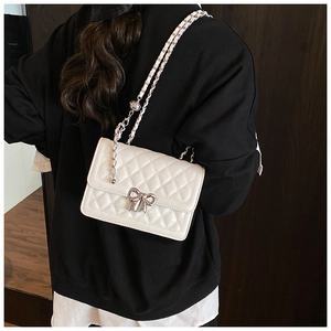 Close-up of white quilted bag with silver bow clasp and chain strap on a model