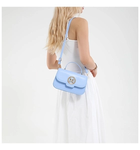 Close-up of light blue crossbody bag with gold M buckle worn by a model in a white dress