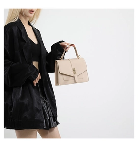 Detalle de bolso crema con cierre de metal dorado llevado por modelo con atuendo negro