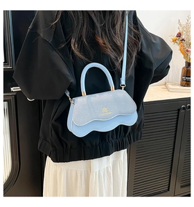 Detail of light blue crossbody bag featuring a wavy base and textured flap with gold logo