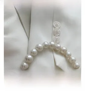 Detail view of the elegant pearl handle with gold metal clasps on a cream handbag