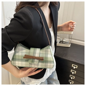 Close-up of green plaid underarm bag featuring a brown leather bow and strap