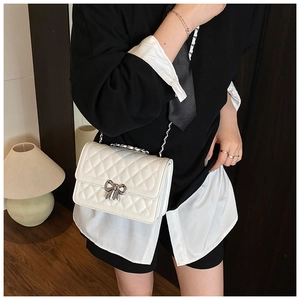 Detail of silver bow clasp and quilted texture on a white chain crossbody bag
