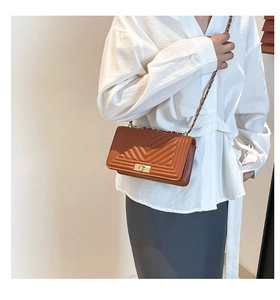 Detailed view of caramel quilted chain crossbody bag styled on a white shirt and grey skirt