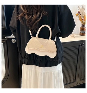 Detail of beige wavy-edge crossbody bag featuring gold logo and semicircular top handle