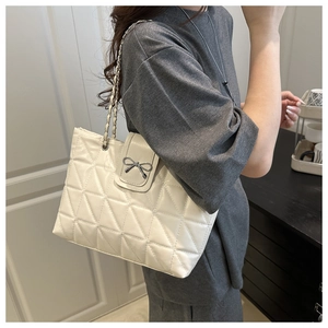 Close-up of white quilted tote bag with silver bow buckle and chain strap detail