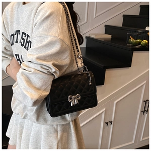 Detail of black quilted chain bag with silver bow clasp worn over a gray hoodie