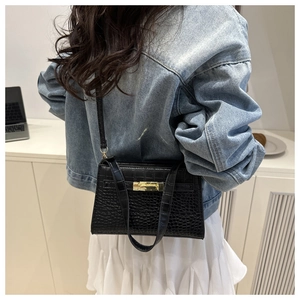 Detail of black crocodile texture handbag with gold lock on a model in a modern room