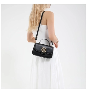 Detail of black crossbody bag with golden M logo worn by model in white dress