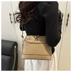 Khaki crossbody bag with textured finish shown on model's shoulder in interior setting