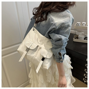 Close-up of white glossy faux leather shoulder bag with dual buckle pockets on a model