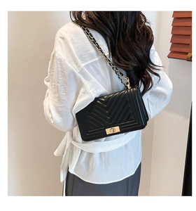 Detail of black quilted shoulder bag with gold hardware and chain strap on a model