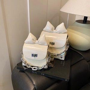Cream white crossbody bag with large bow and woven texture on a book-top setup