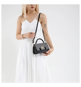 Detail of grey and black crossbody bag with gold M logo on a model in white dress