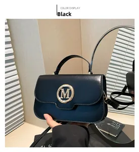 Detail of classic black leather tote bag with gold M-logo buckle and top handle