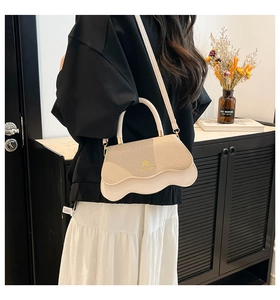 Detail of elegant cream handbag featuring wavy base design and gold metal logo accent