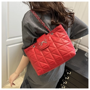 Close-up of red quilted tote bag with chain strap and silver bow detail worn by model