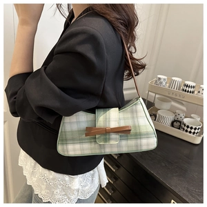 Detail of green plaid baguette bag with a brown bow accessory worn by a model