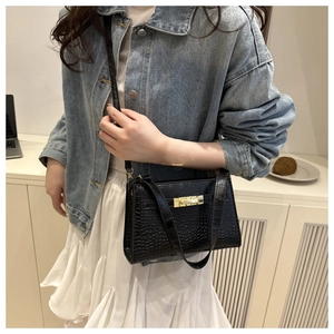 Detail of black crocodile pattern shoulder bag featuring a gold buckle on model
