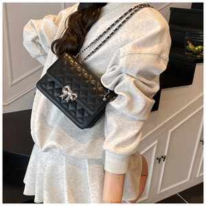 Detail of silver bow metal lock and diamond quilted texture on black crossbody bag