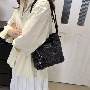Sac à bandoulière chic en paillettes noires porté par un mannequin en tenue élégante