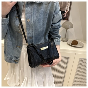 Detail of black crocodile texture crossbody bag with metal lock shown on person