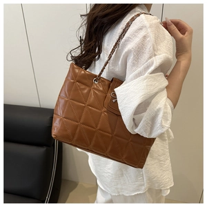 Detail of caramel brown quilted tote bag with silver chain strap worn by a model
