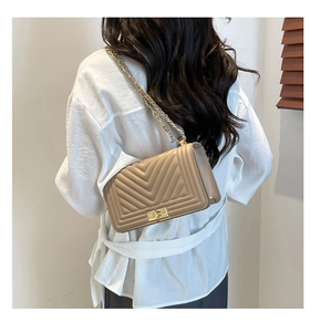 Detail of beige quilted shoulder bag with gold chain strap worn by model against shutters