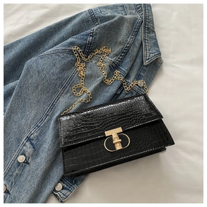 Close-up of black crocodile pattern leather bag with golden T-shape lock and chain strap