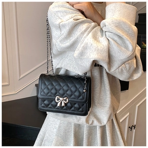 Detail of black quilted crossbody bag with silver bow buckle and metal chain strap