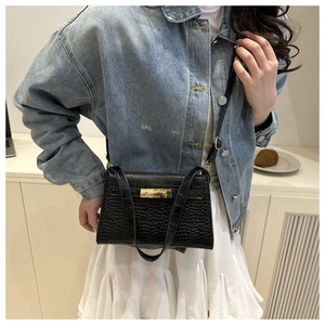 Close-up of black quilted shoulder bag with gold twist lock on a casual model outfit