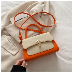 Detail of color-block handbag with orange leather and beige fabric texture on white blazer