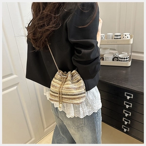 Détail d'un sac seau en paille avec rayures dorées, bandoulière chaîne et pompon perle