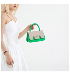 Detail of green leather handbag featuring beige canvas flap and golden M buckle