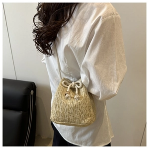Detail of hand-woven straw bucket bag with white drawstring closure and metal accents
