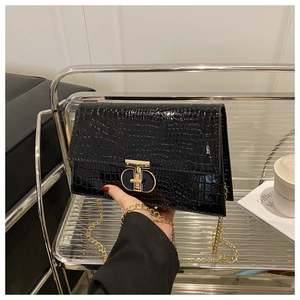 Detail of black crocodile pattern flap bag with gold metal buckle and chain strap