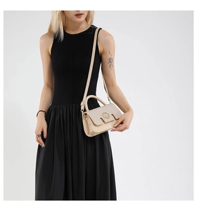 Detailed view of beige crossbody bag with a circular metal M buckle on black dress