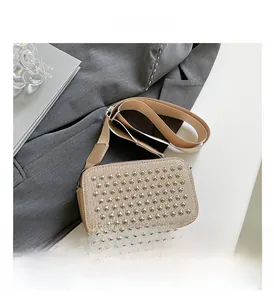Close-up of textured khaki crossbody bag featuring golden cone studs and wide strap
