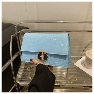 Detail of light blue crocodile pattern flap bag with golden rotating metal lock and chain