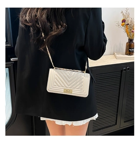 White quilted shoulder bag with gold chain strap and turn-lock closure on black blazer