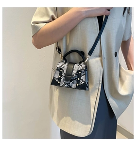 Detail of snake skin pattern handbag featuring gold rivets and black leather trim