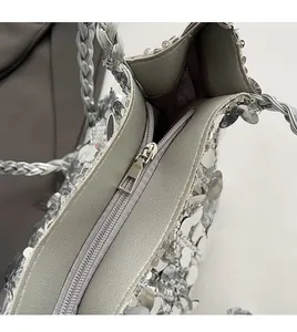 Detail of silver sequin tote bag showing smooth metal zipper and braided leather handle