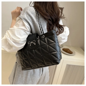 Detailed close-up of black quilted tote bag with silver bow charm and chain strap