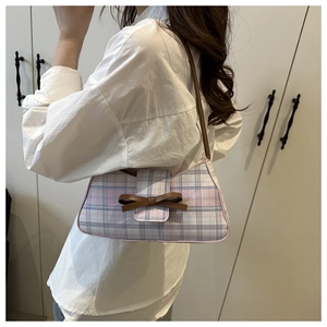 Close-up of a plaid baguette bag featuring a leather bow and brown shoulder strap